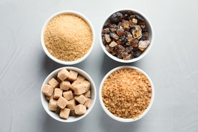 Bowls with different types of sugar on gray background