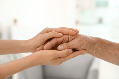 People holding hands together on blurred background, closeup. Help and elderly care concept