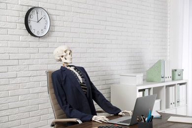 Human skeleton in suit using laptop at table in office