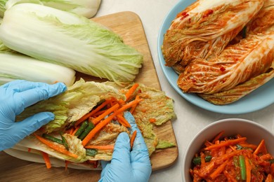 Woman preparing spicy cabbage kimchi at beige marble table, top view