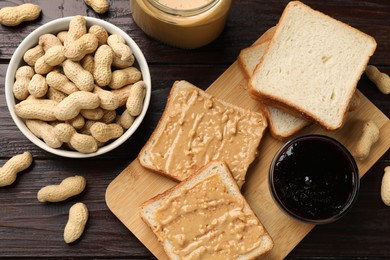 Photo of Delicious toasts with peanut butter, nuts and jam on dark wooden table, flat lay