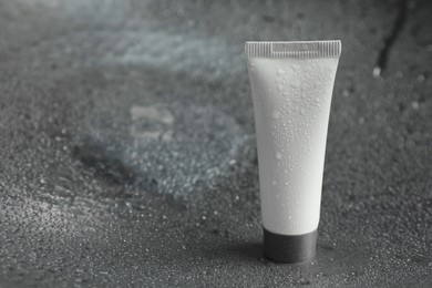 Photo of Moisturizing cream in tube on dark wet background, closeup. Space for text