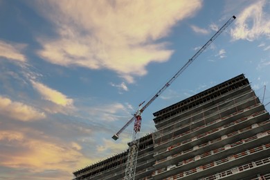 Construction site with tower crane near unfinished building against beautiful cloudy sky, low angle view