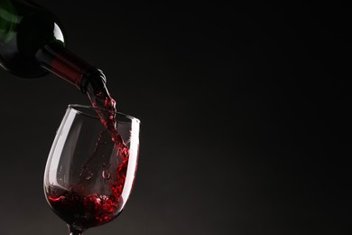 Photo of Pouring tasty red wine from bottle into glass on dark background, closeup. Space for text
