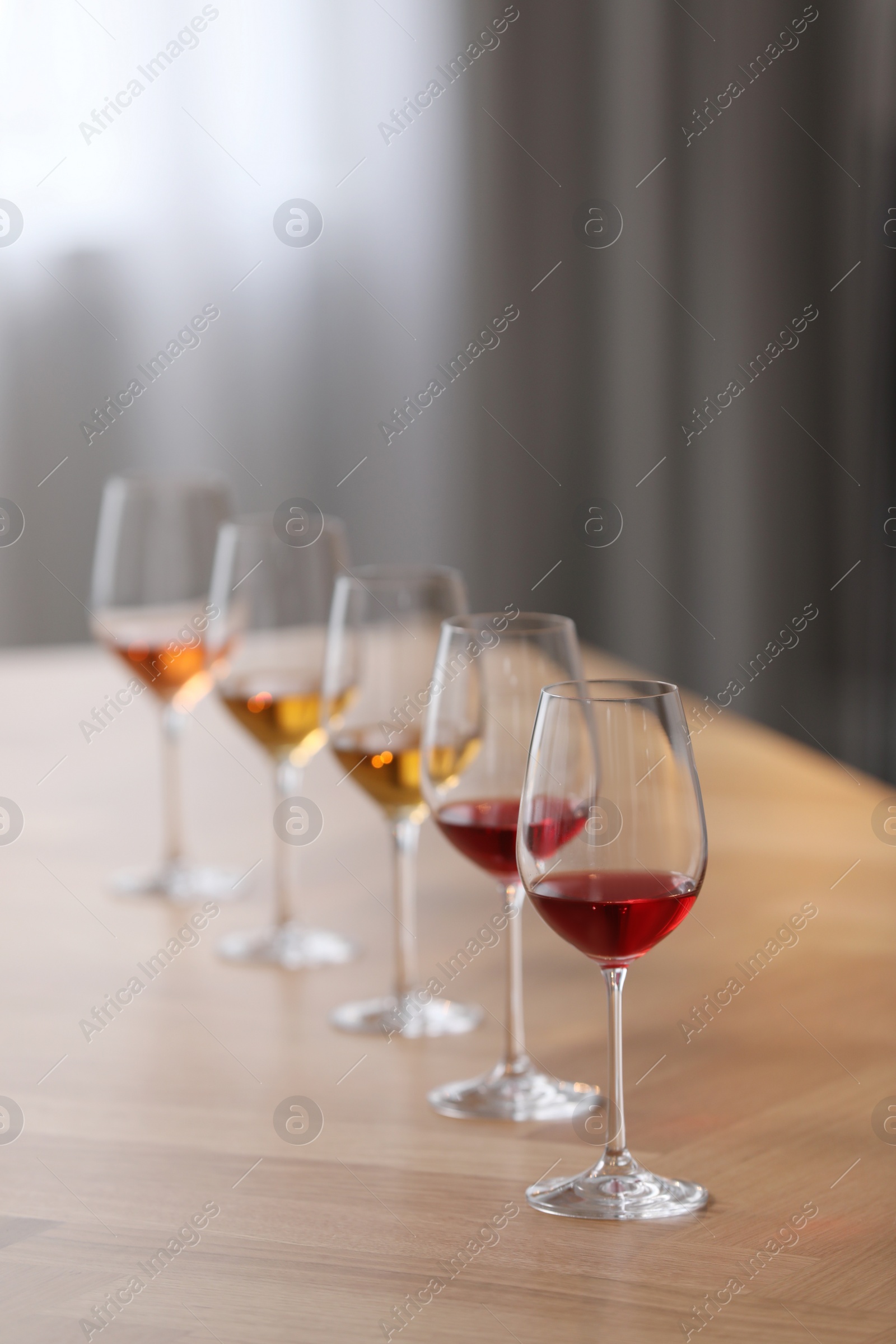 Photo of Different sorts of wine in glasses prepared for tasting on wooden table indoors