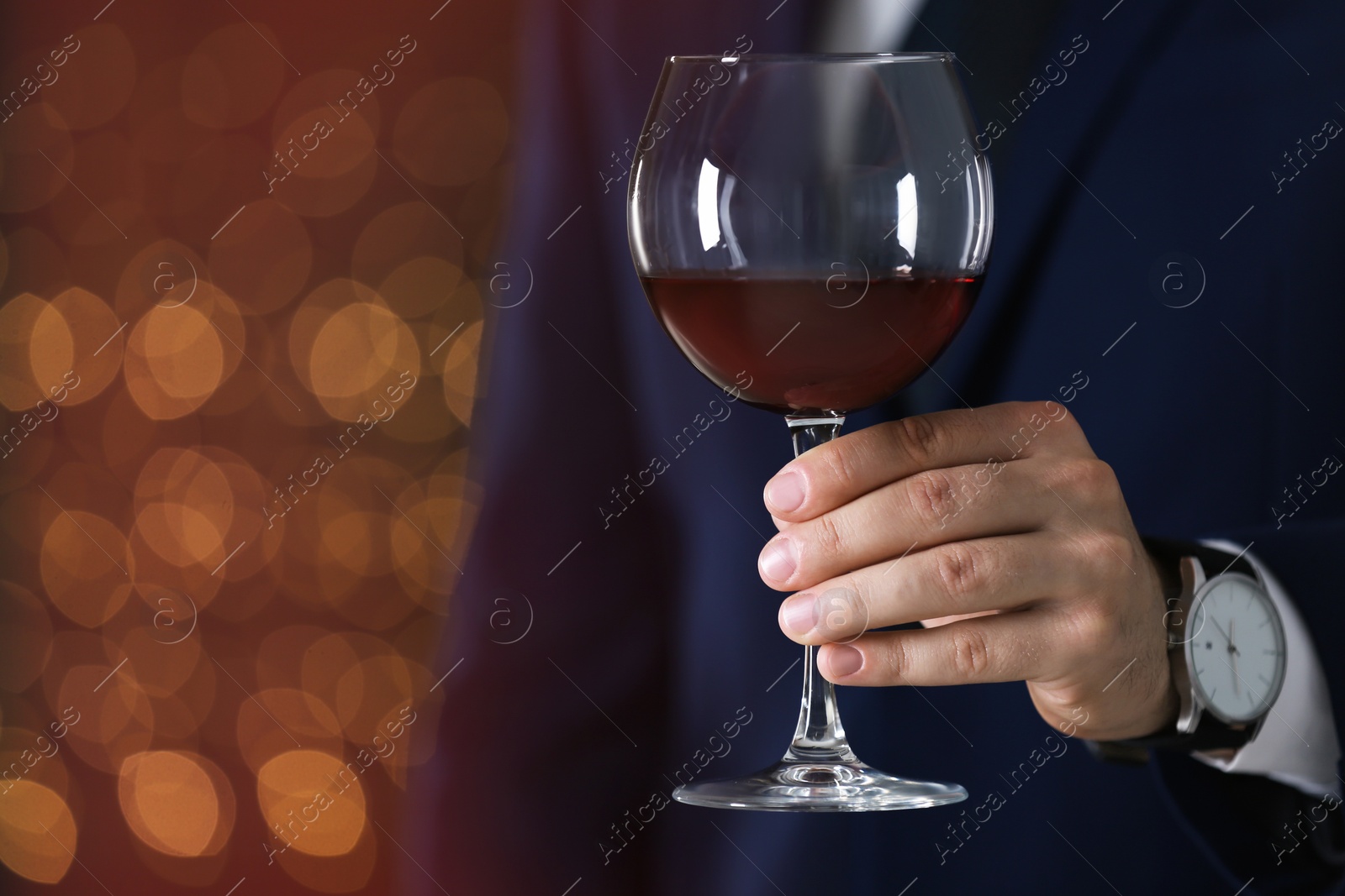 Photo of Man in formal suit with glass of wine against blurred background, closeup. Space for text