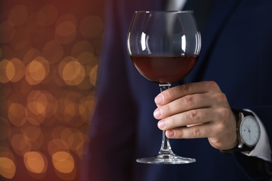 Photo of Man in formal suit with glass of wine against blurred background, closeup. Space for text