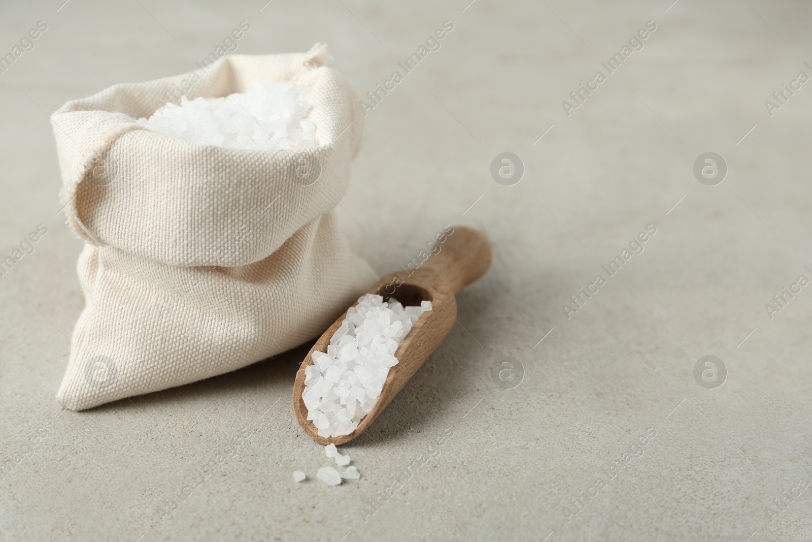 Photo of Wooden scoop and bag with natural sea salt on light table, space for text