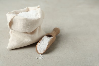 Wooden scoop and bag with natural sea salt on light table, space for text