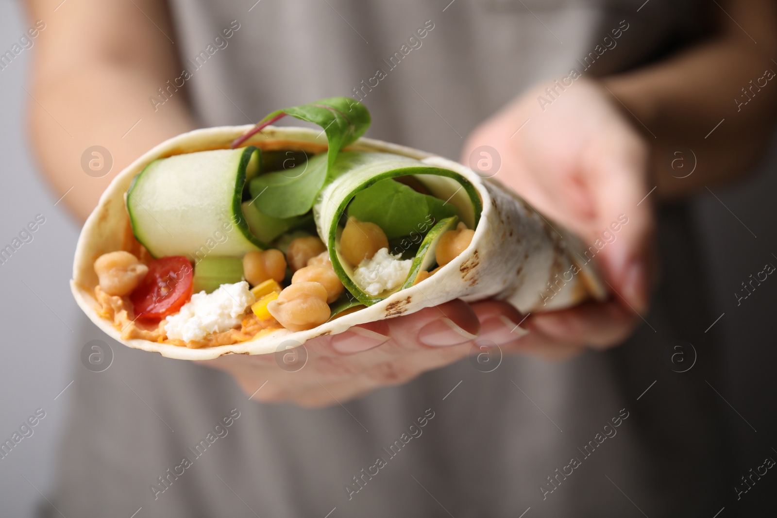 Photo of Woman holding delicious hummus wrap with vegetables, closeup