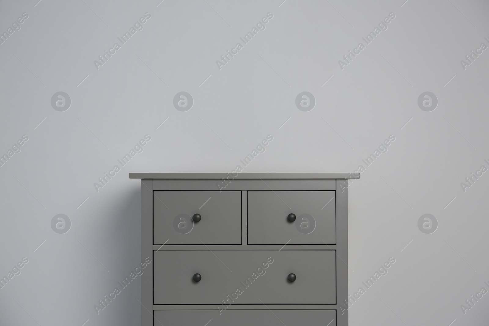 Photo of Grey chest of drawers on light background. Space for text