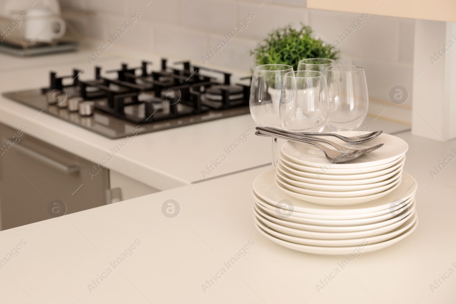 Photo of Stack of clean dishes, glasses and cutlery on table in kitchen. Space for text