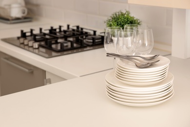 Photo of Stack of clean dishes, glasses and cutlery on table in kitchen. Space for text