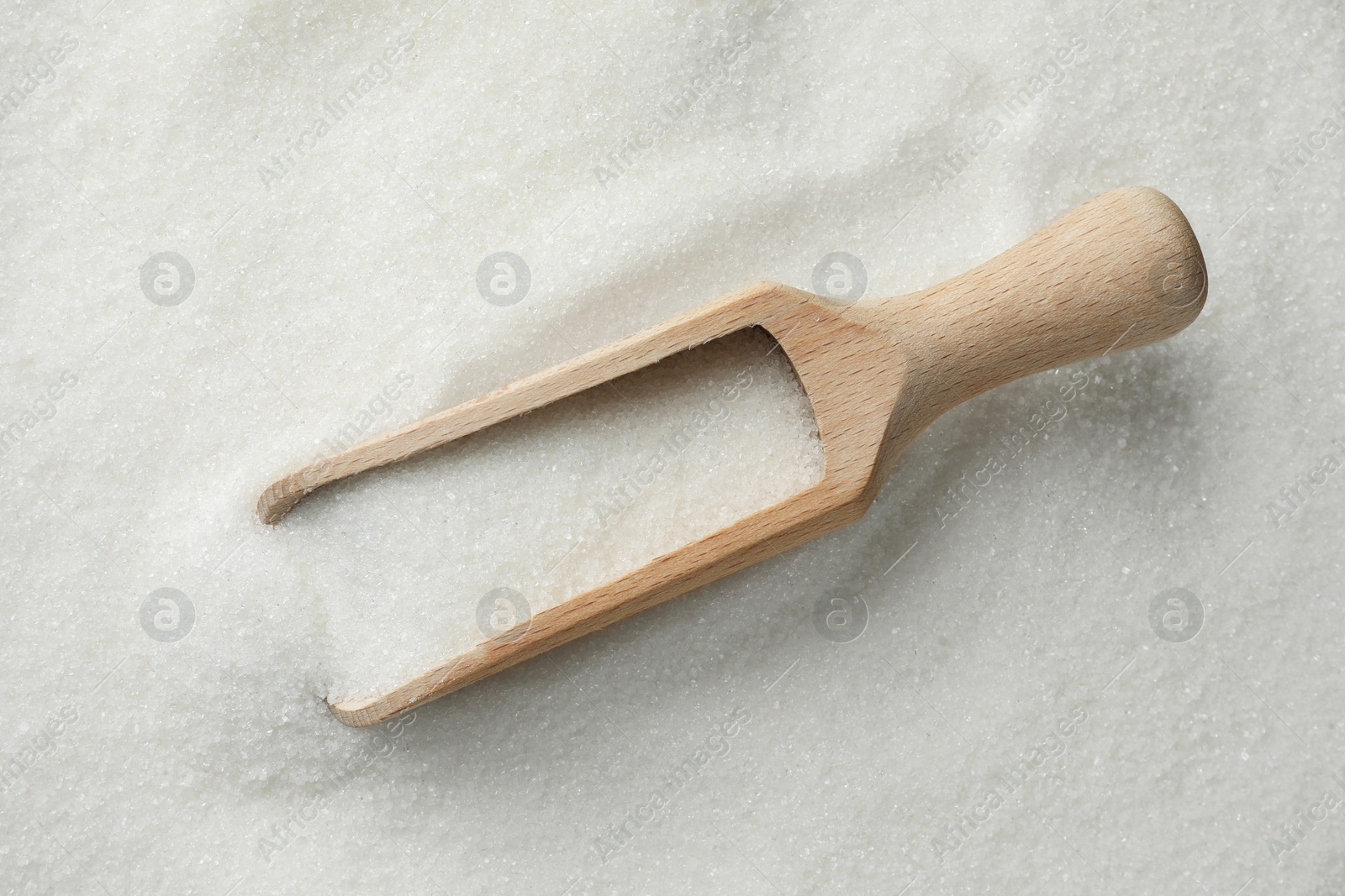 Photo of Wooden scoop on granulated sugar, top view