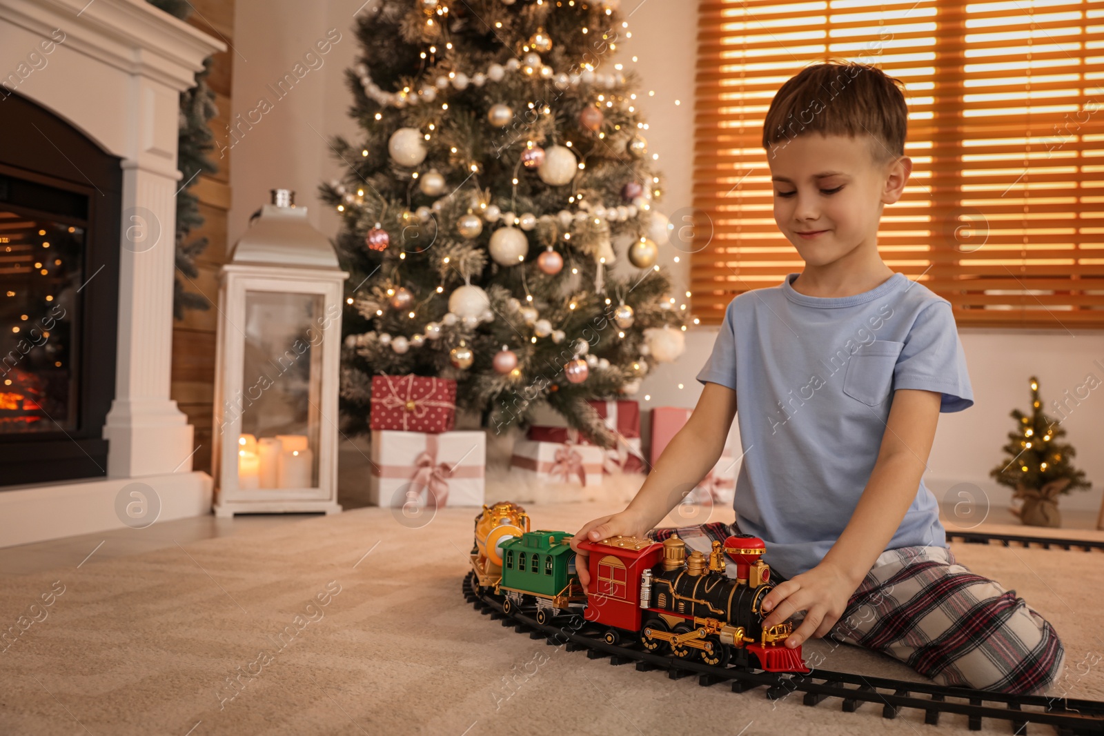 Photo of Little boy playing with colorful train toy in room decorated for Christmas