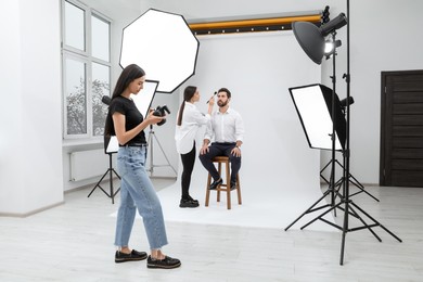 Professional photographer and stylist working with model in modern photo studio