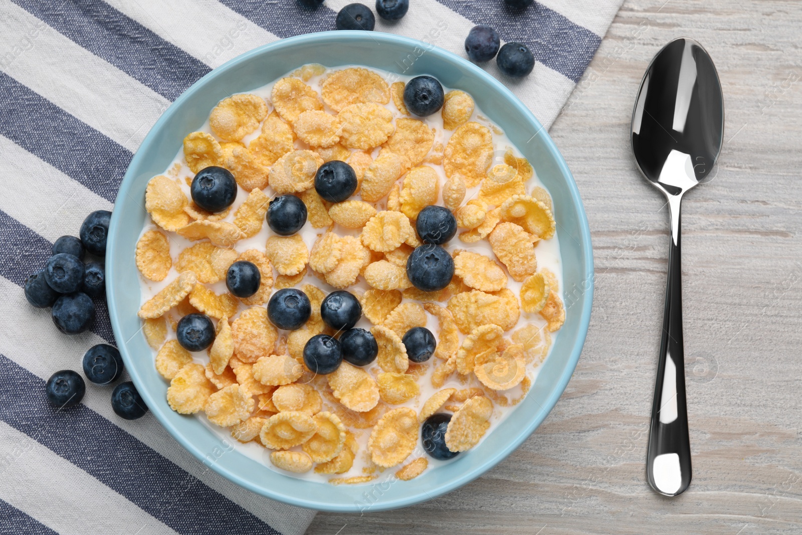 Photo of Bowl of tasty crispy corn flakes with milk and blueberries on wooden table, flat lay
