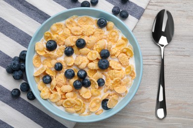 Bowl of tasty crispy corn flakes with milk and blueberries on wooden table, flat lay