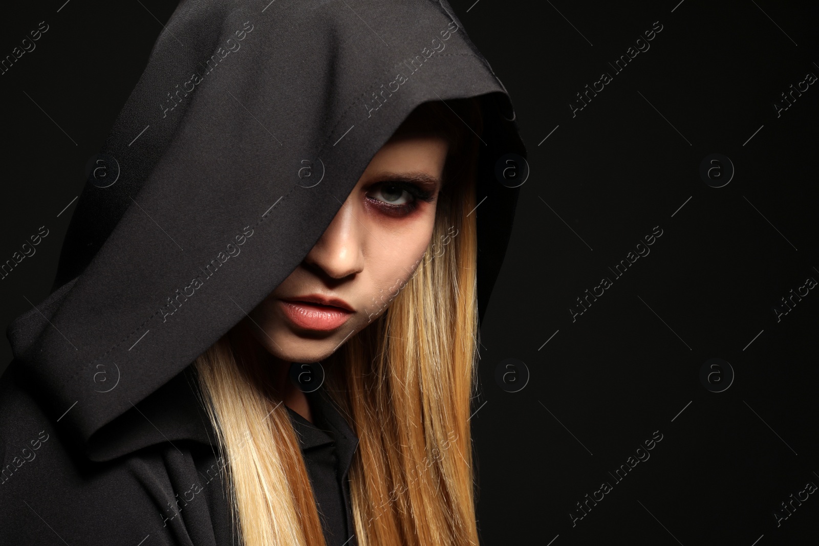 Photo of Witch in black mantle on dark background. Scary fantasy character