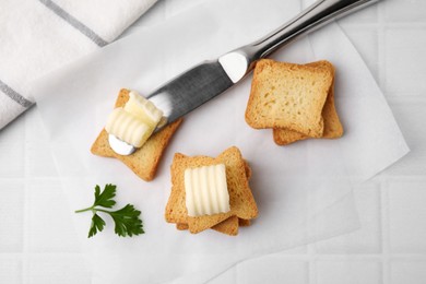 Tasty butter curls, knife and pieces of dry bread on white tiled table, flat lay