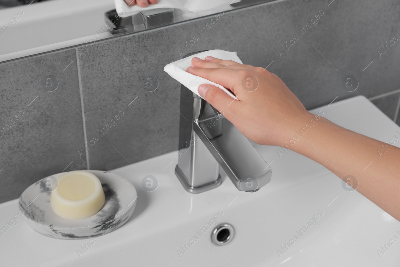 Photo of Woman cleaning faucet of bathroom sink with paper towel, closeup