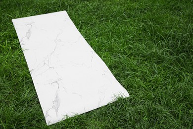 Photo of White karemat or fitness mat on green grass outdoors. Space for text