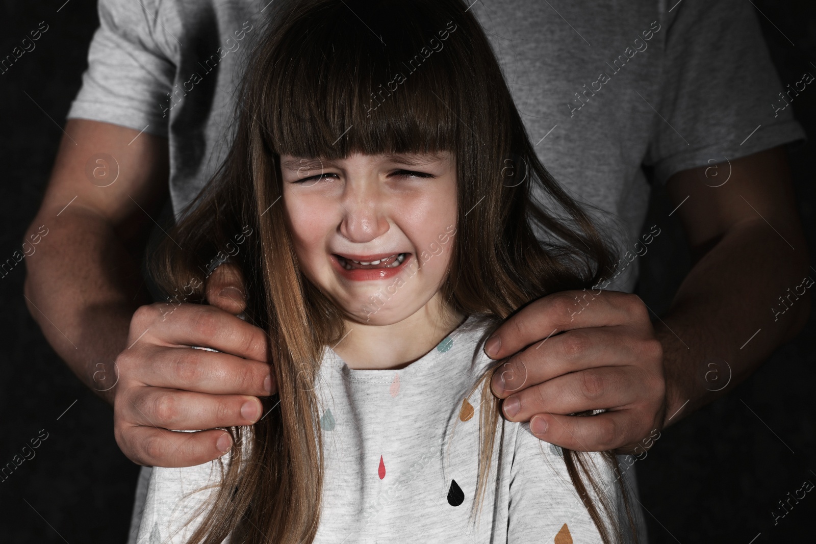 Photo of Crying little girl and adult man on dark background, closeup. Child in danger