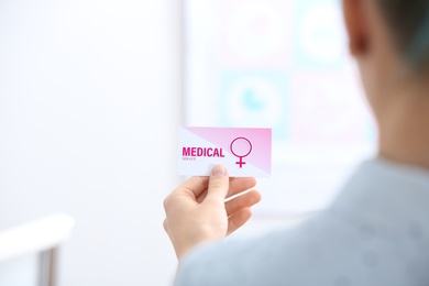 Photo of Girl holding medical business card indoors, closeup. Women's health service