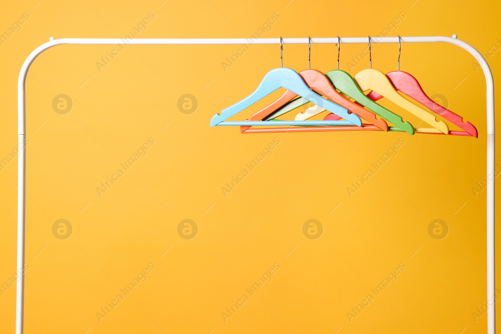 Photo of Bright clothes hangers on metal rack against yellow background