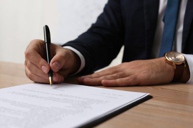 Photo of Businessman signing contract at wooden table indoors, closeup