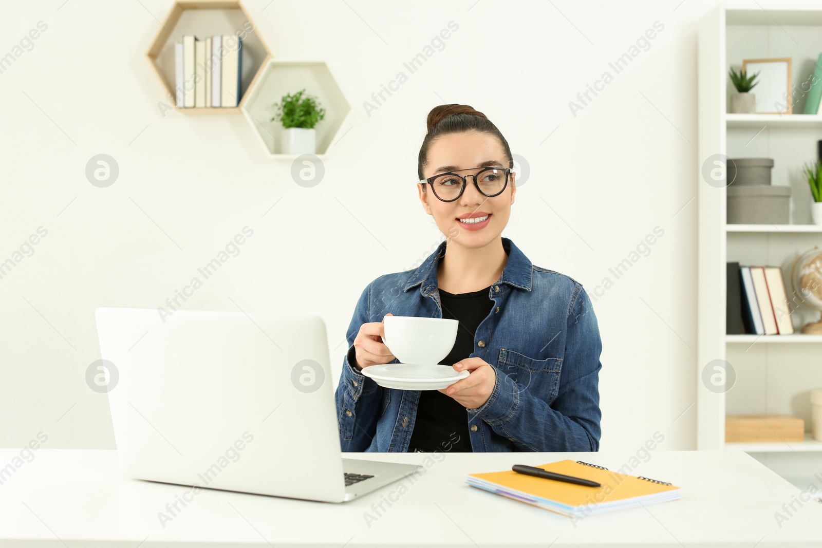 Photo of Home workplace. Happy woman with cup of hot drink near laptop at white desk in room