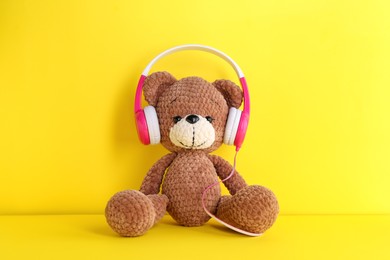 Baby songs. Toy bear in headphones on yellow background