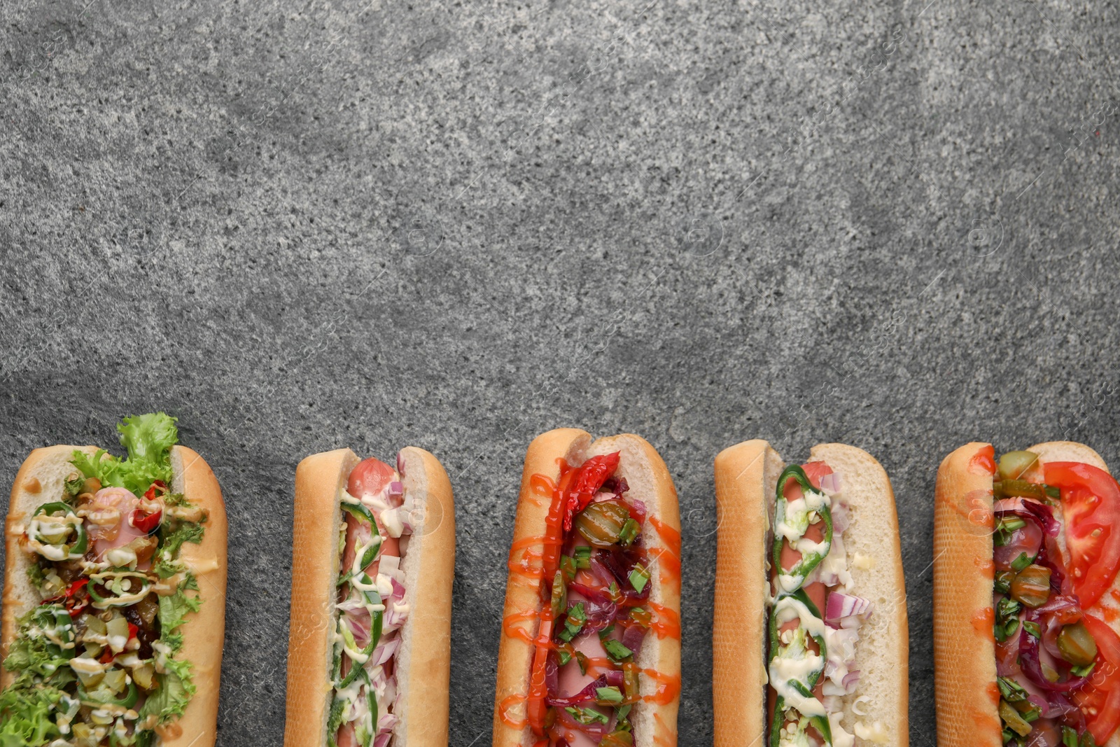 Photo of Delicious hot dogs with different toppings on grey table, flat lay. Space for text