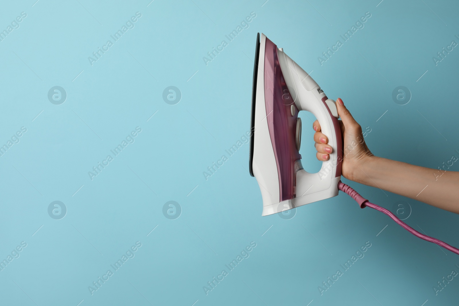 Photo of Woman holding modern iron on turquoise background, closeup. Space for text