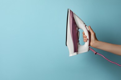 Photo of Woman holding modern iron on turquoise background, closeup. Space for text