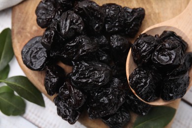 Photo of Spoon with tasty dried prunes and green leaves on light wooden table, top view