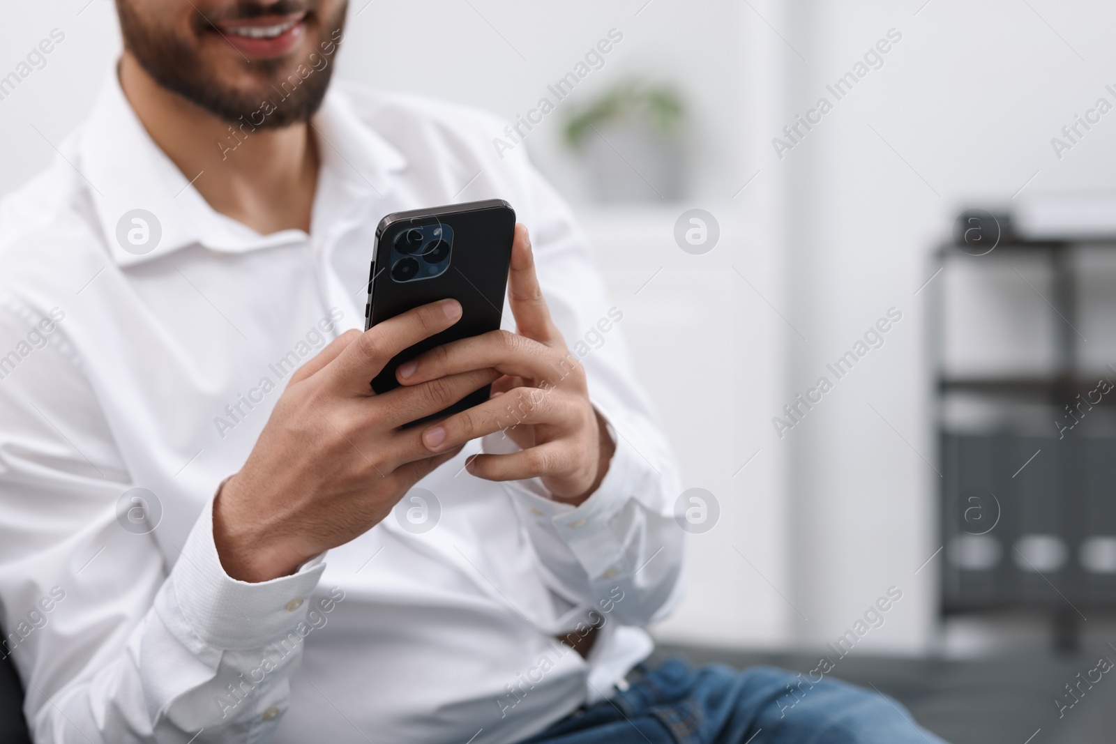 Photo of Young man using smartphone in office, closeup. Space for text