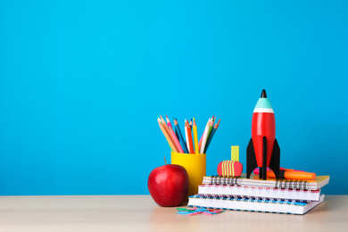 Photo of Bright toy rocket and school supplies on wooden desk. Space for text