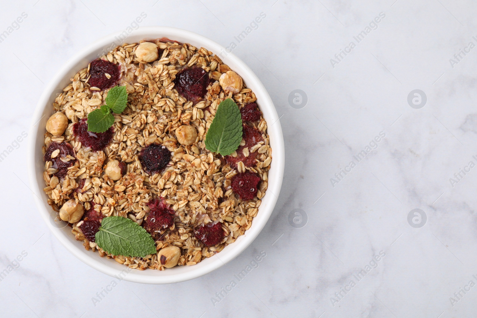 Photo of Tasty baked oatmeal with berries and nuts on white marble table, top view. Space for text