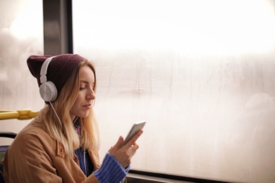 Photo of Young woman with headphones listening to music in public transport, space for text