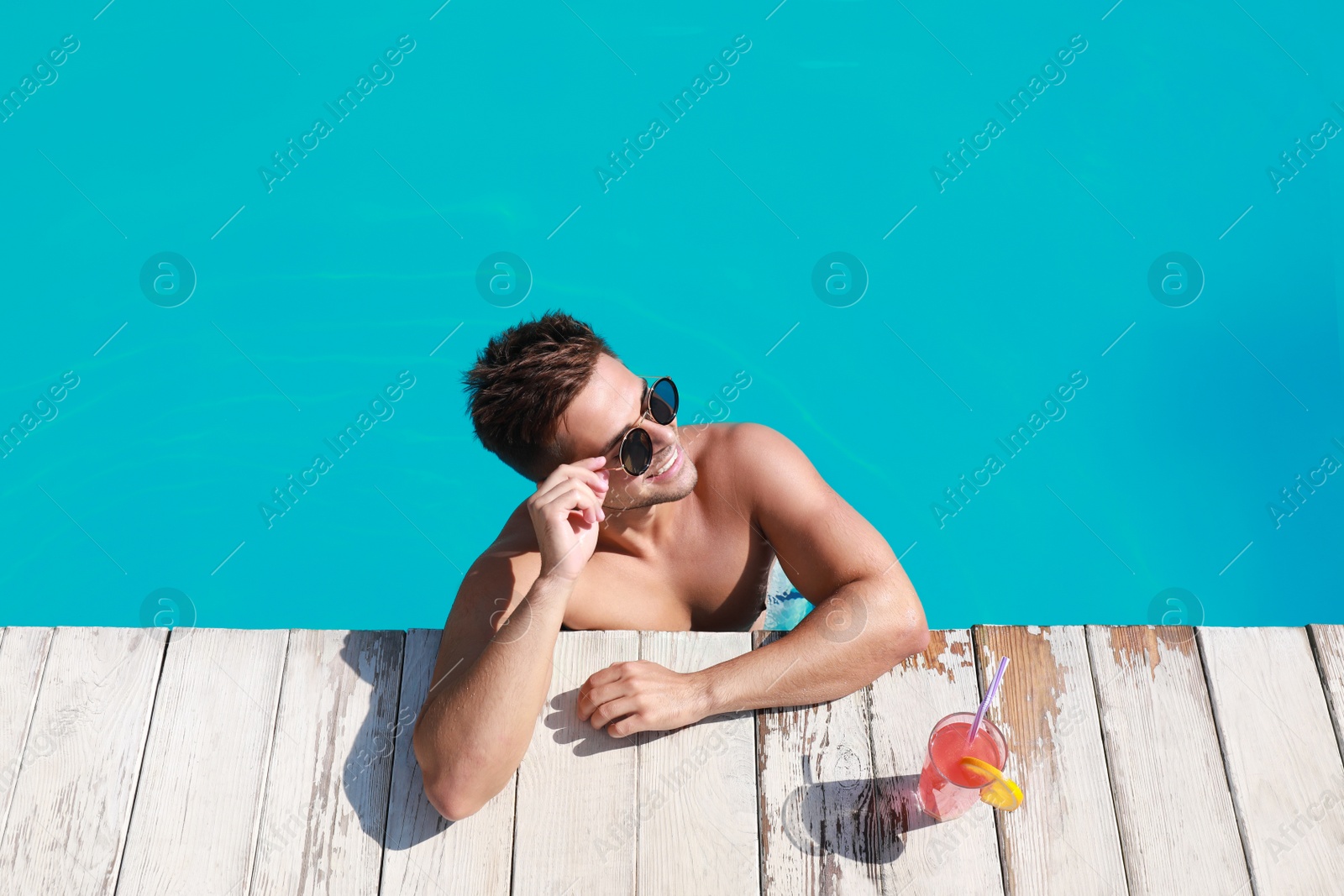 Photo of Handsome young man with refreshing cocktail in swimming pool on sunny day, above view