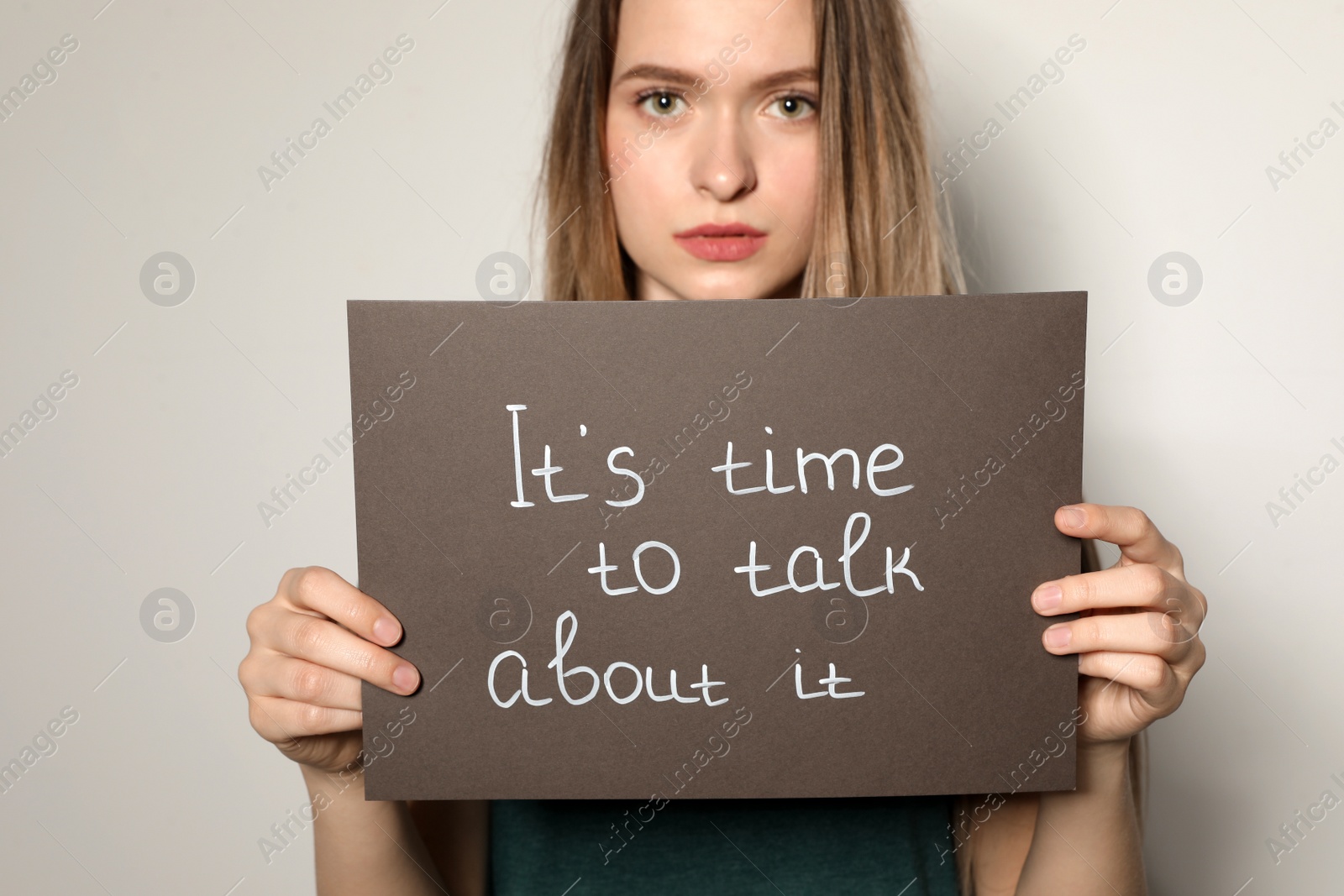 Photo of Young woman holding card with words IT'S TIME TO TALK ABOUT IT against light background