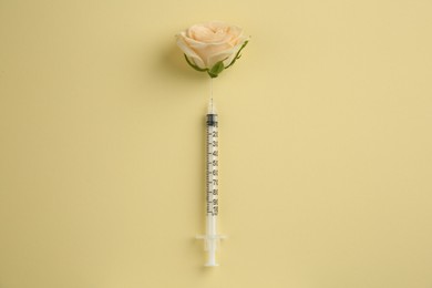 Photo of Medical syringe and beautiful rose on pale yellow background, top view