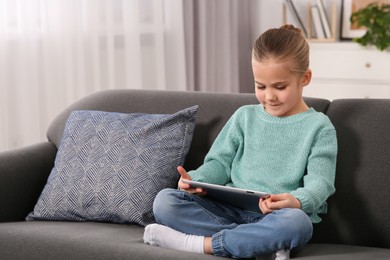 Little girl using tablet on sofa at home. Internet addiction