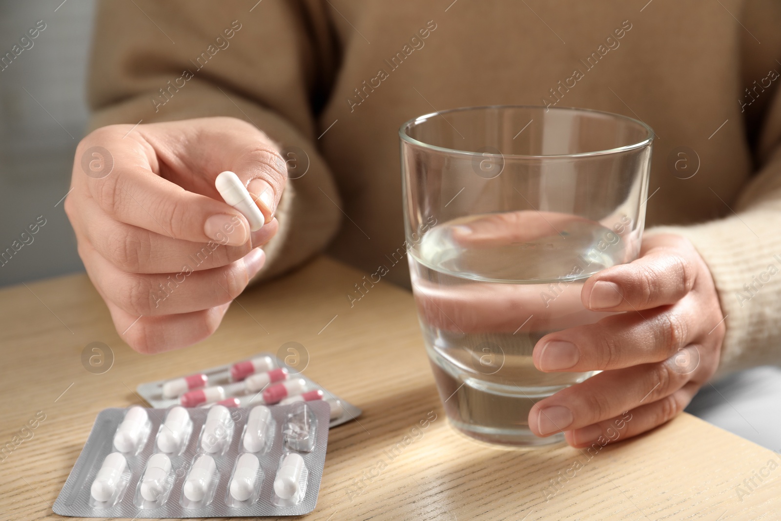 Photo of Woman with glass of water and pill at wooden table, closeup