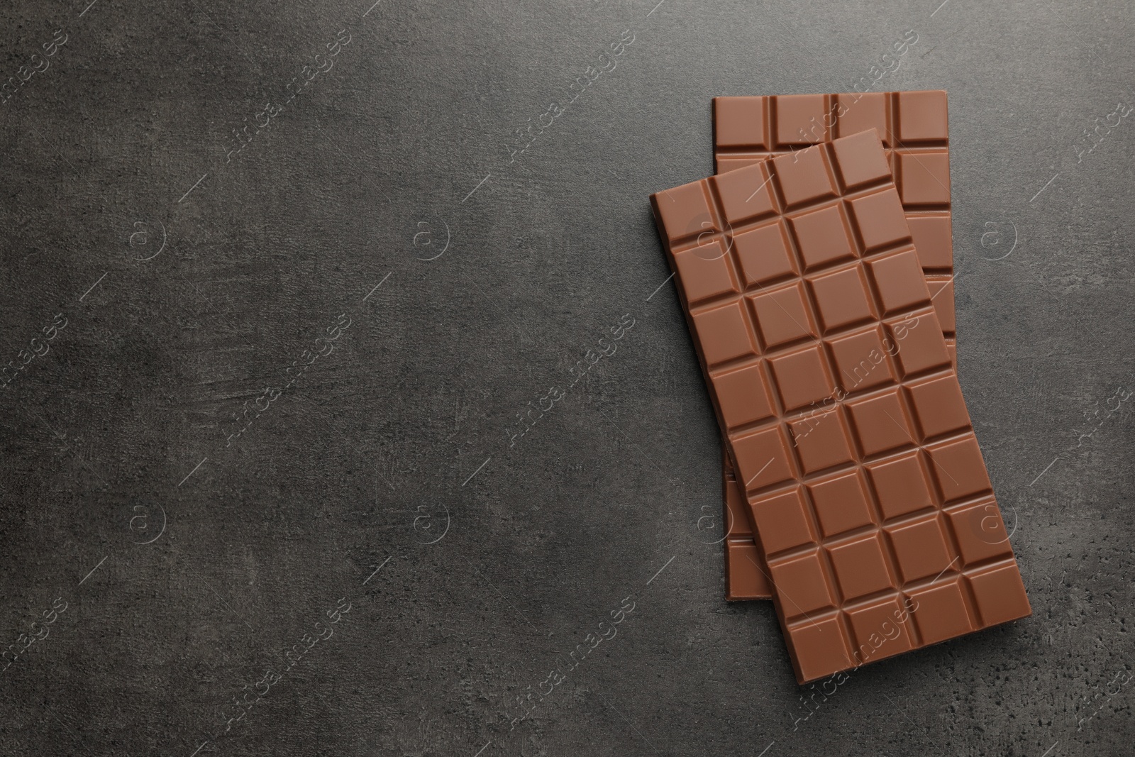 Photo of Delicious milk chocolate bars on black table, flat lay. Space for text