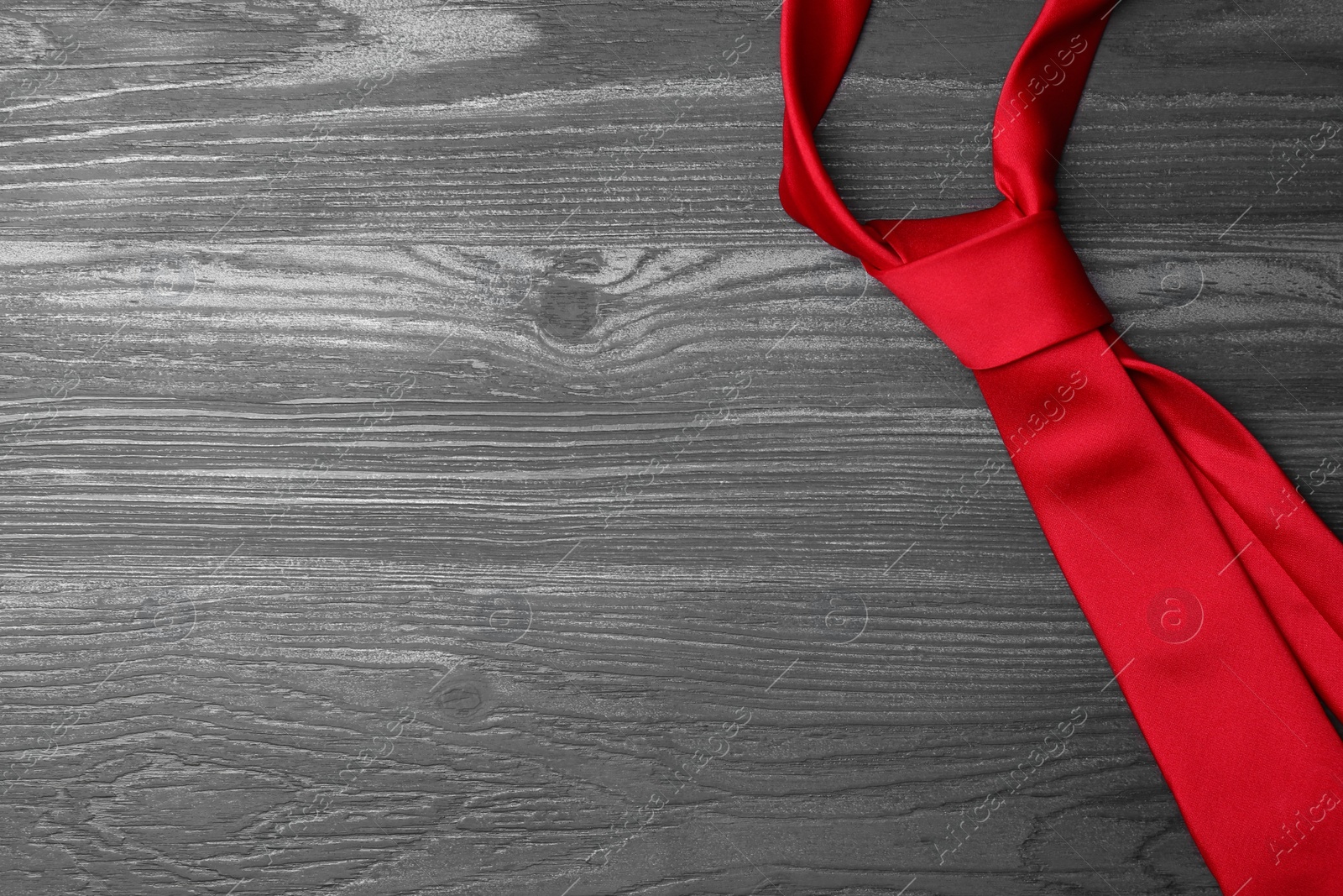 Photo of Stylish red silk necktie on dark grey wooden table, top view with space for text