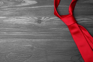 Photo of Stylish red silk necktie on dark grey wooden table, top view with space for text