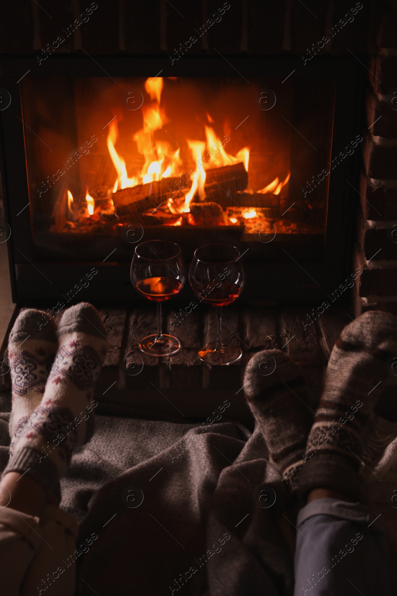 Photo of Couple and glasses of red wine near burning fireplace, closeup