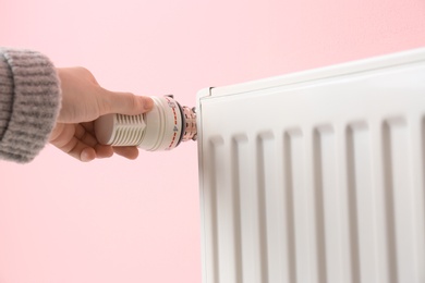 Photo of Woman adjusting heating radiator against color background